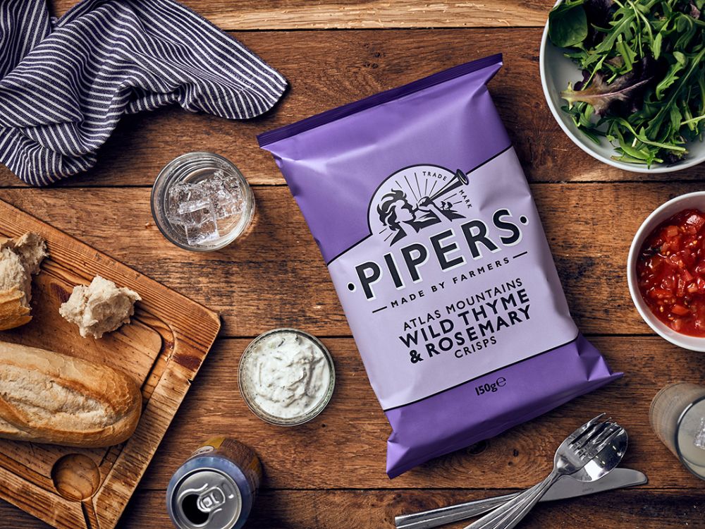 a packet of Wild Thyme and Rosemary Pipers crisps on a wooden breakfast table.
