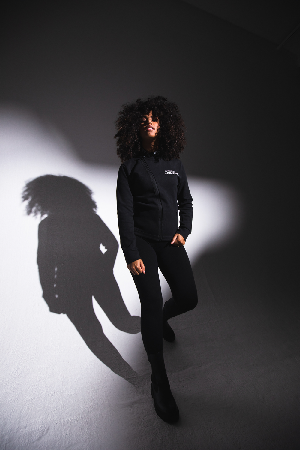 Woman in black Yamaha clothes with, looking straight into the camera, lit up with a spotlight.