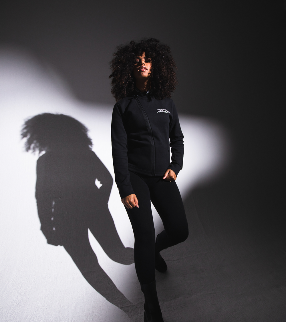 Woman in black Yamaha clothes with, looking straight into the camera, lit up with a spotlight.