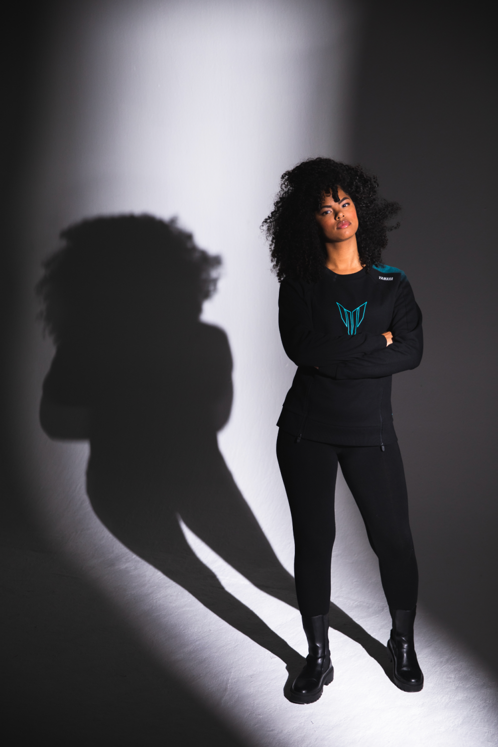 Black woman in Yamaha clothes with blue colors, looking straight into the camera, lit up with a spotlight.