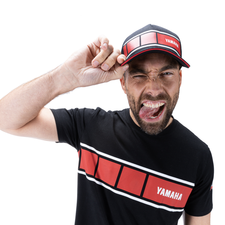 Man close up to camera pulling a cheeky face with black Yamaha hat and tshirt, both with red stripe across.