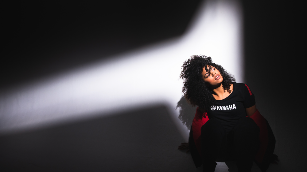 Black woman in Yamaha clothes, looking up with spotlight shining on her.