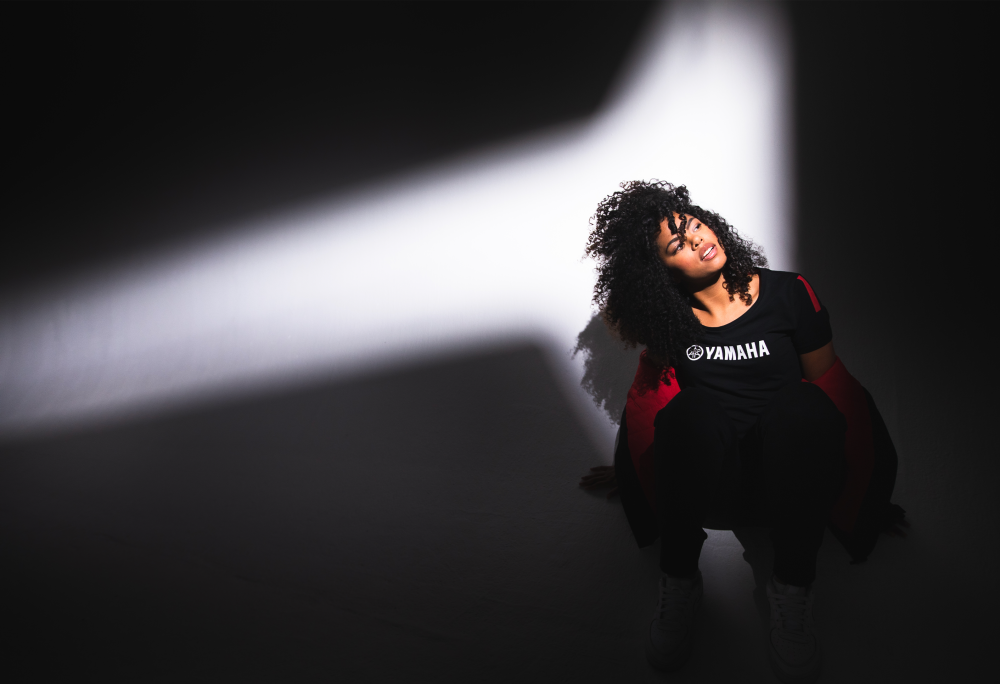 Black woman in Yamaha clothes, looking up with spotlight shining on her.