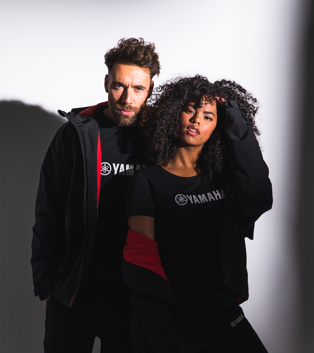 Man and woman with Yamaha clothes posing casually against a spotlight.
