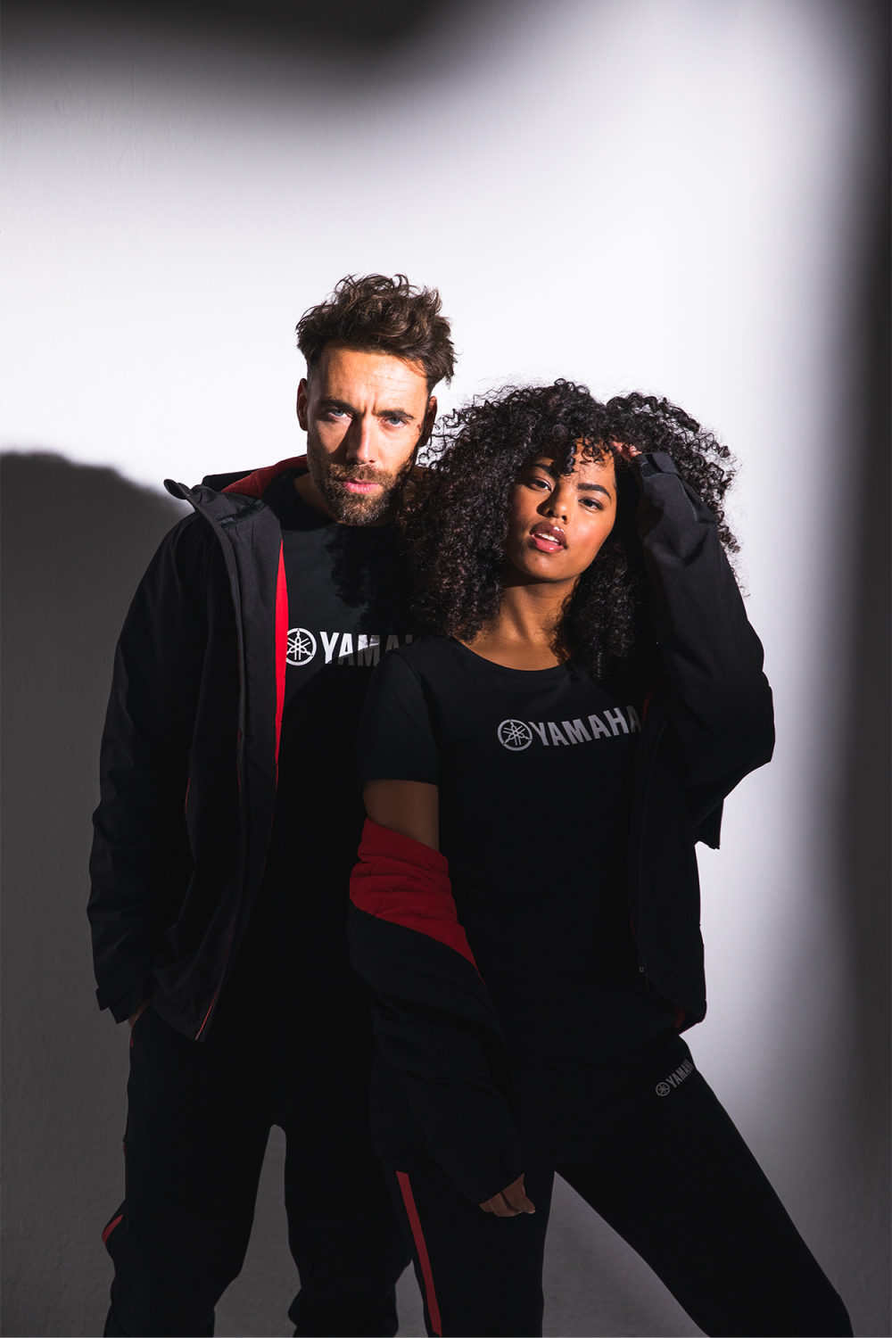 Man and woman with Yamaha clothes posing casually against a spotlight.
