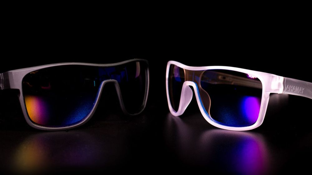 A pair of black glasses and a pair of white glasses facing each other with neon reflections.