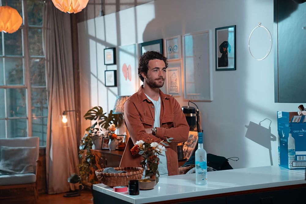 A man casually standing at an apartment kitchen bar in front of Grey Goose vodka.