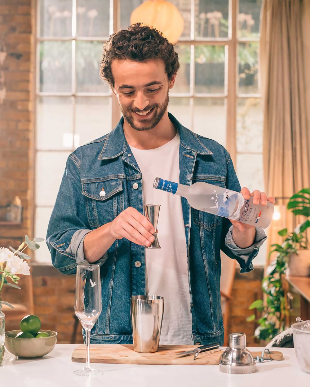 Man pouring Grey Goose in an apartment with a denim jacket.