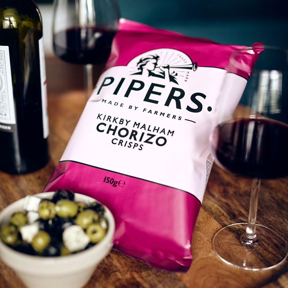 Pipers Kirkby Malham Chorizo crisps on a table with red wine and olives.