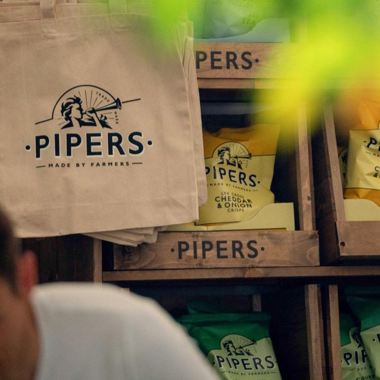 Pipers crisps in a farm box on a shelf with a tote bag hanging next to it.