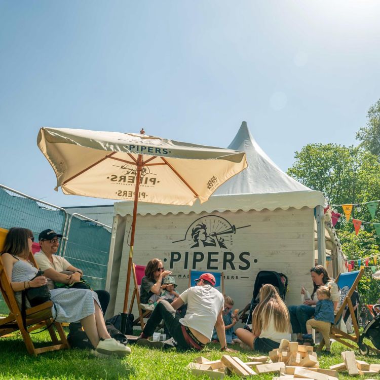 Pipers Crisps stall with various teenagers sitting on the grass under the sun.