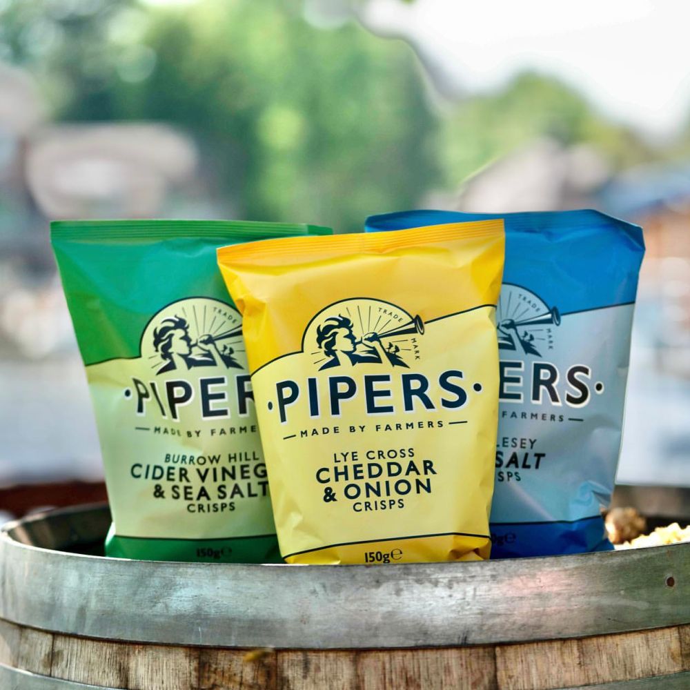 Three different Pipers Crisps flavours sticking out of a popcorn with a bokeh background.
