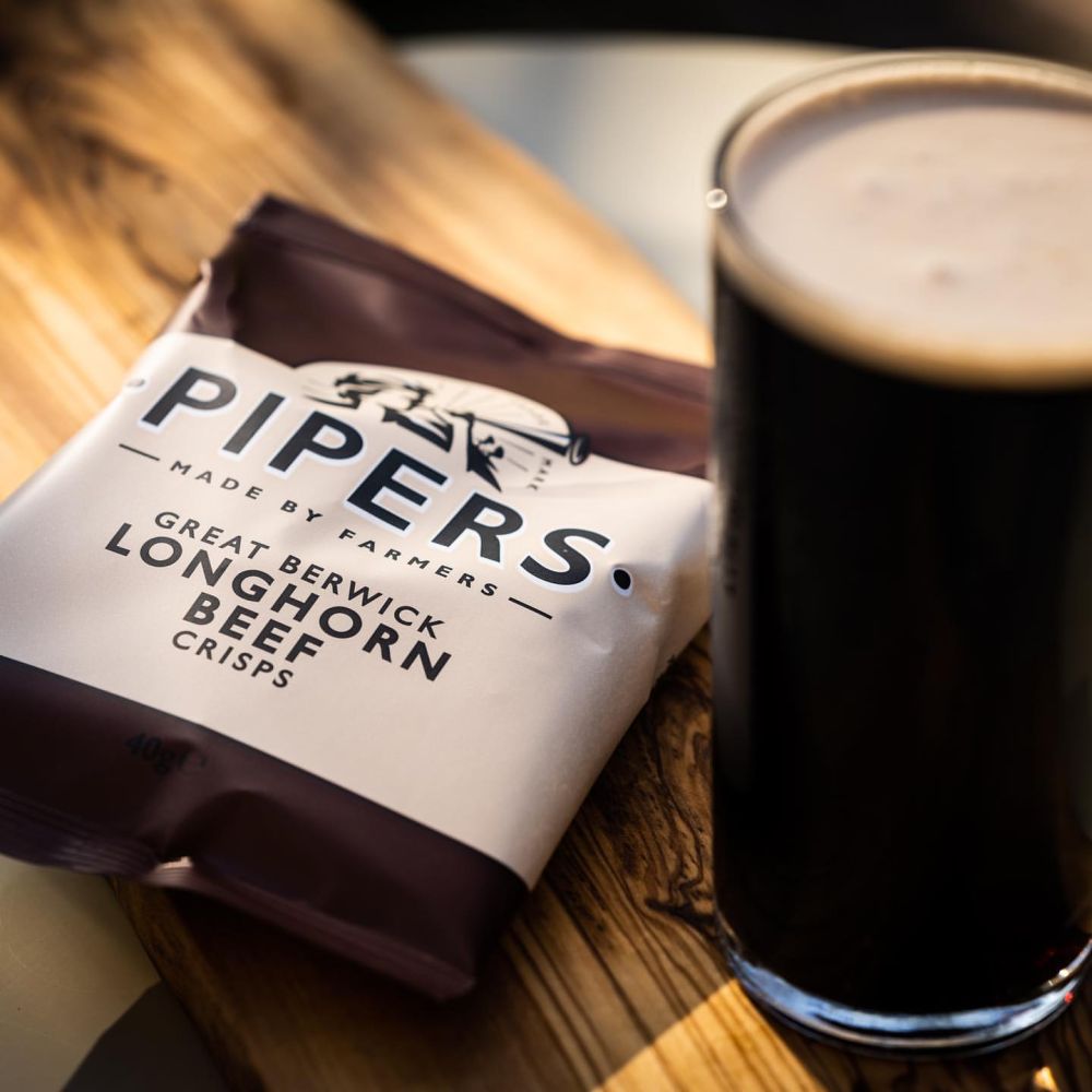Pipers Great Berwick Longhorn Beef crisps on a table with a stout.