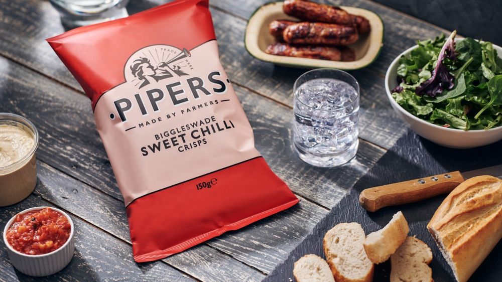 Pipers Sweet Chilli flavour shown on a lunch table with bread, salad, water, and various dips.