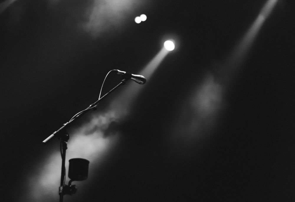 A lone mic in black and white on stage with dry ice and spotlights.