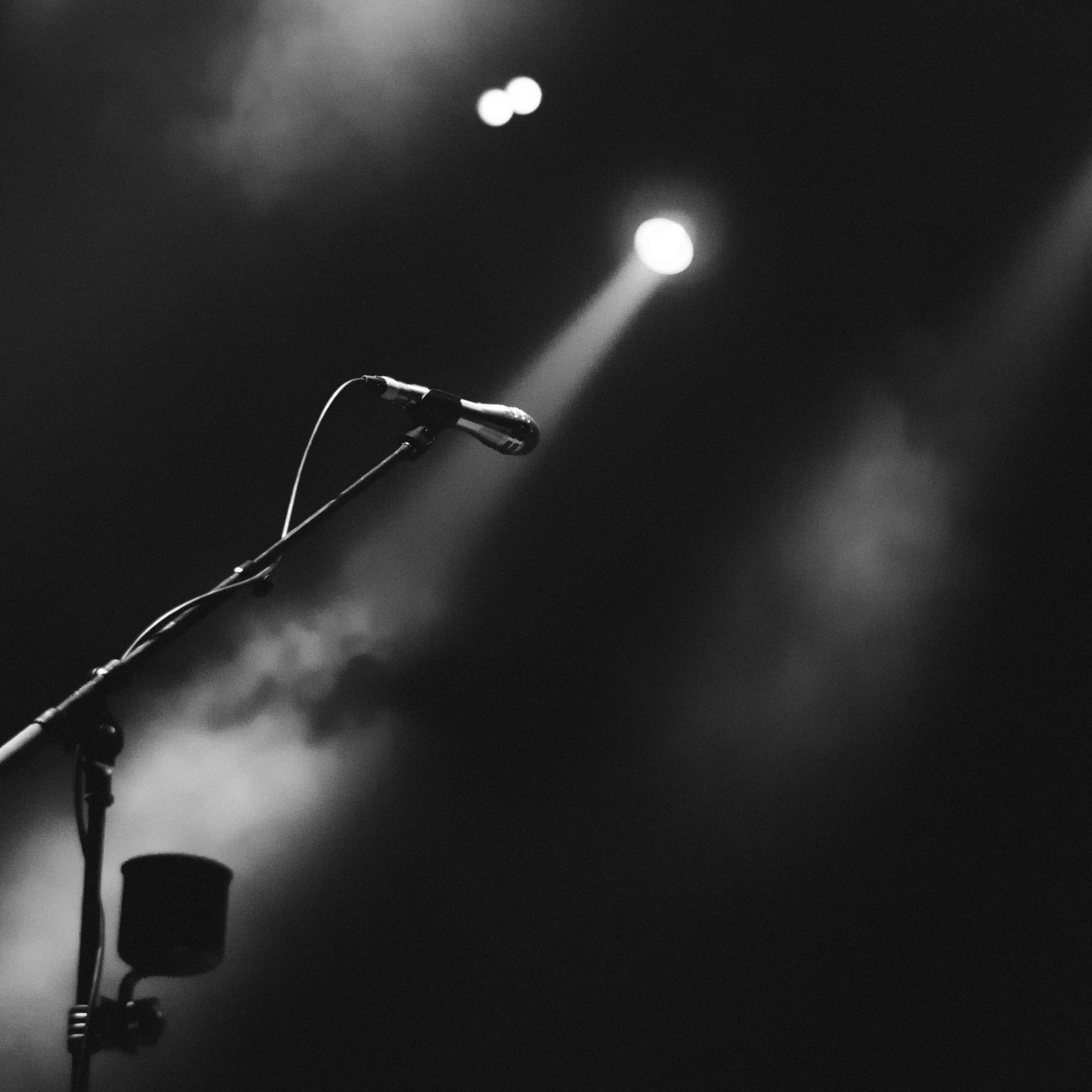 A lone mic in black and white on stage with dry ice and spotlights.