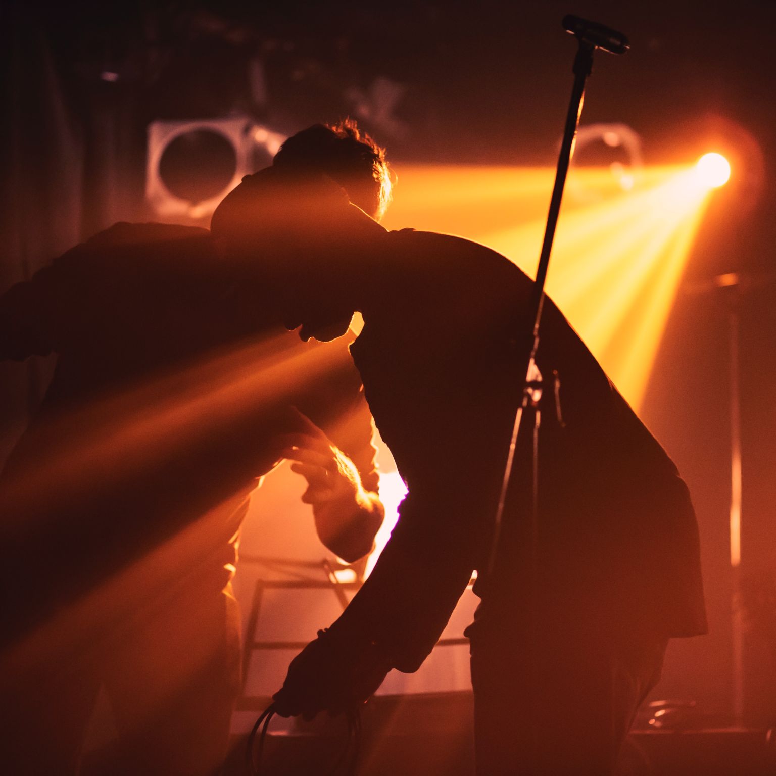 Musician setting up in low orange light with a mic in the foreground.