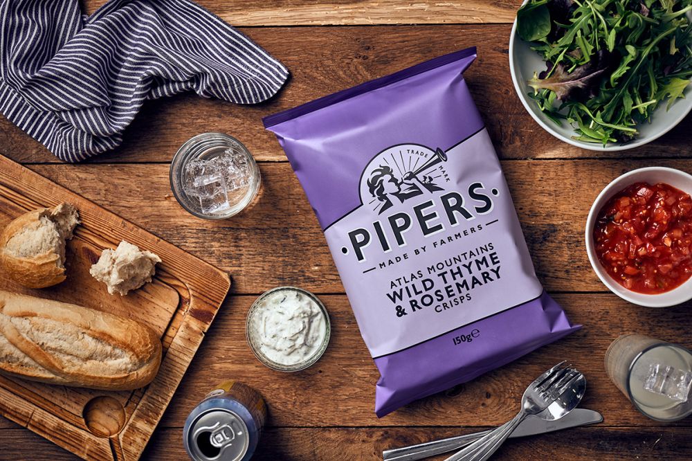 a packet of Wild Thyme and Rosemary Pipers crisps on a wooden breakfast table.