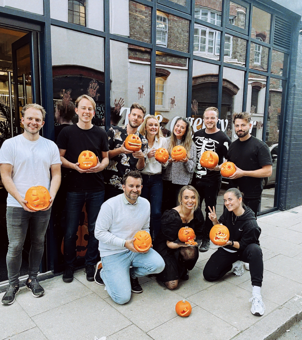 The Paradise team outside the office for Halloween 2021 holding up their carved pumpkins.