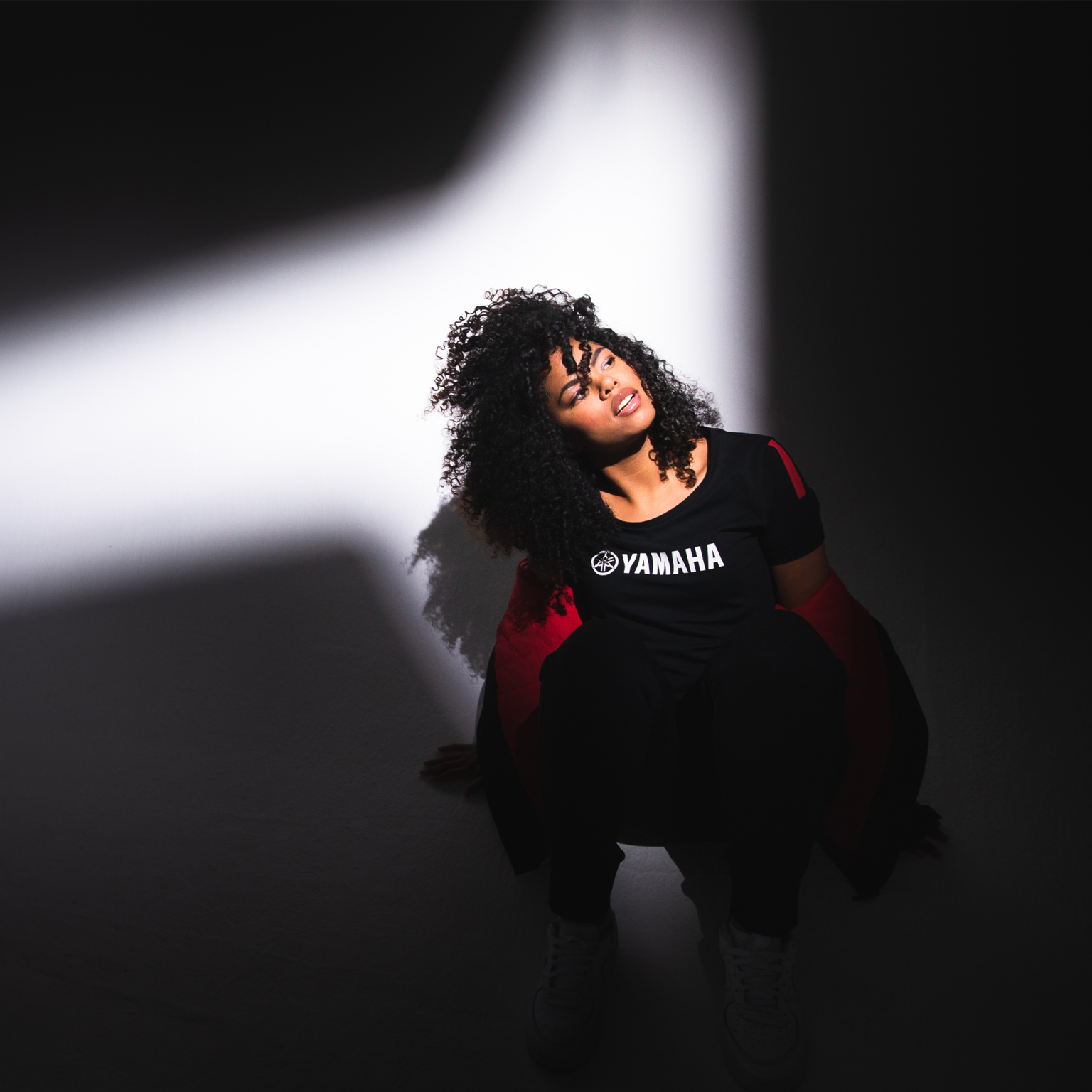 Black woman in Yamaha clothes, looking up with spotlight shining on her.