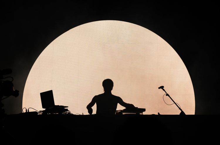 Shadow of a DJ behind a sunset-like screen.