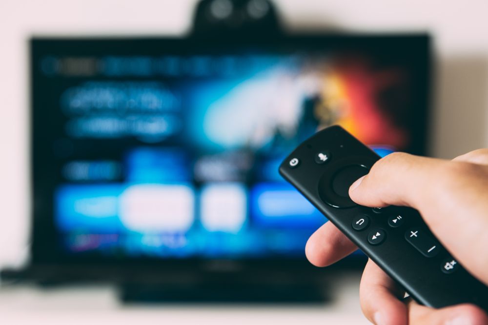 A tv remote showing a TV blurred in the background.