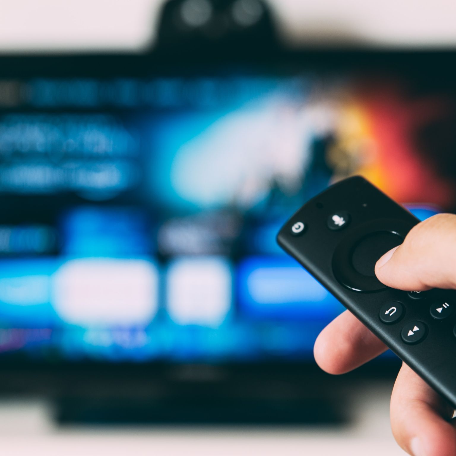 A tv remote showing a TV blurred in the background.