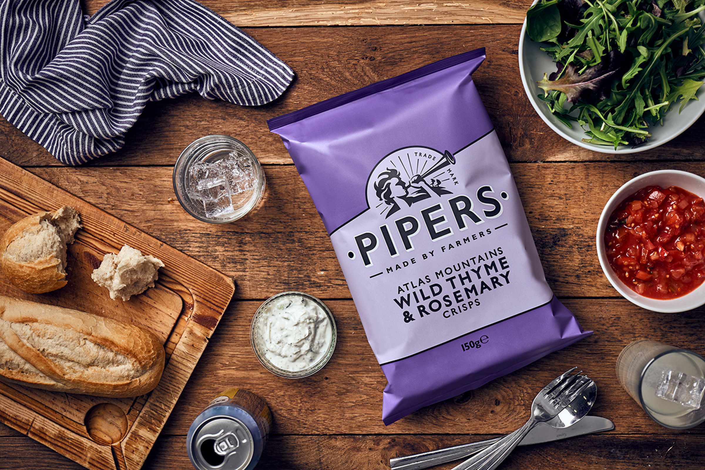 a packet of Wild Thyme and Rosemary Pipers crisps on a wooden breakfast table.