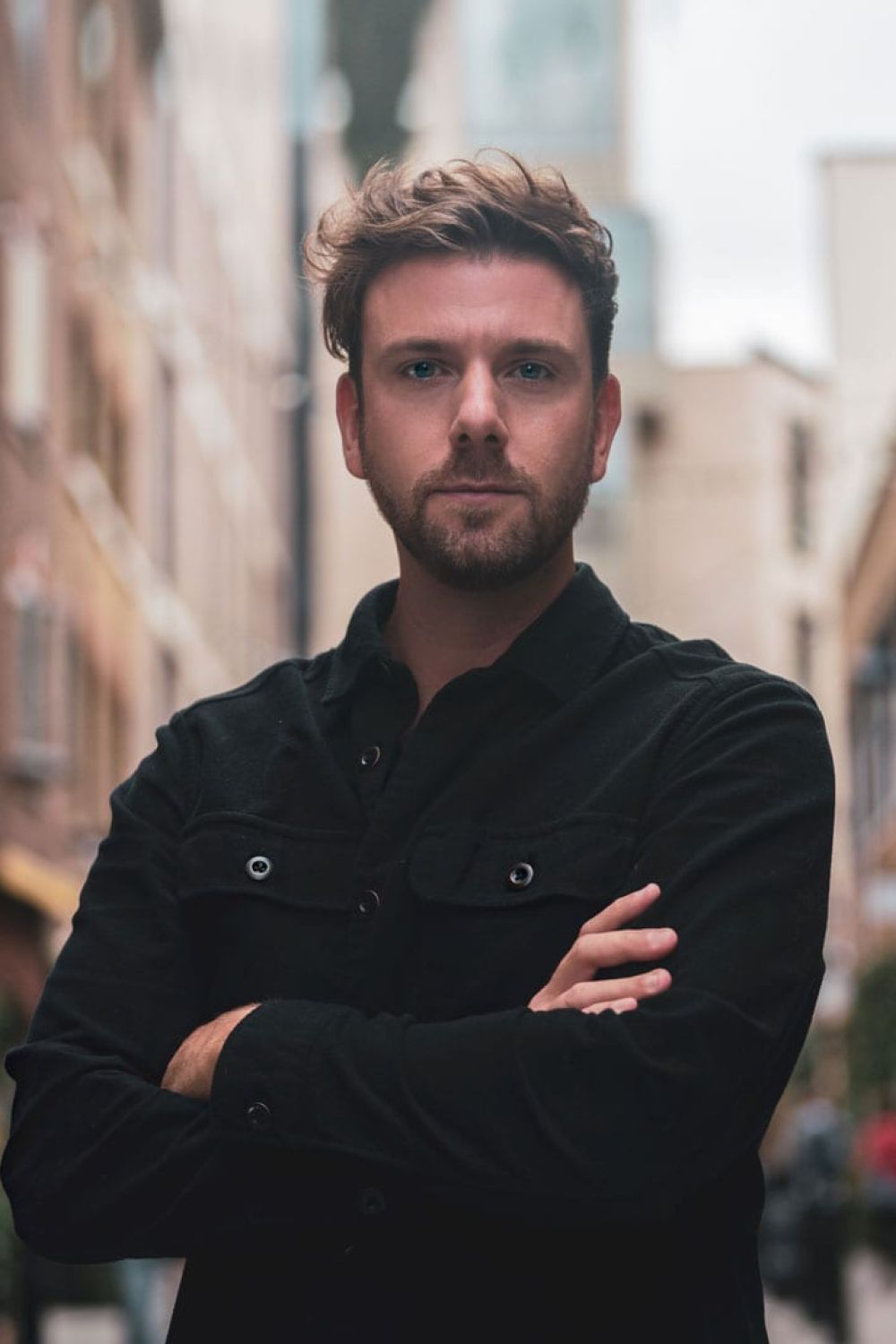 Nick Jekyll wearing a black jacket with arms folded, the street blurred behind him.